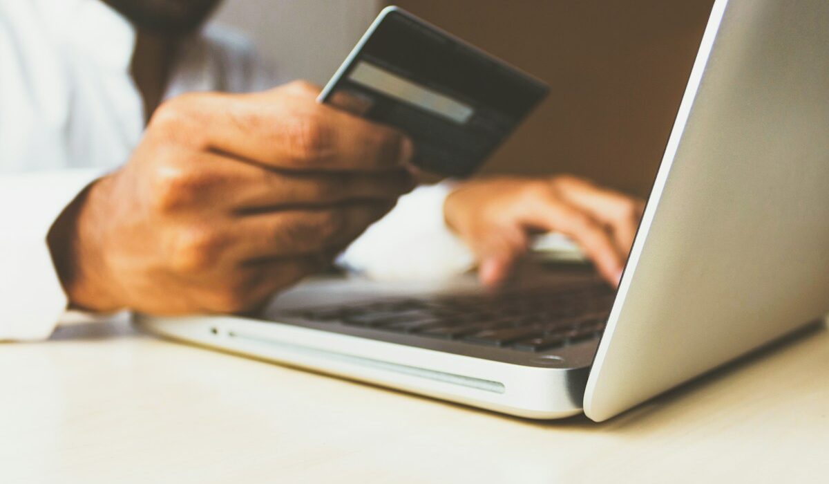 Person holding a credit card beside a laptop for an online purchase