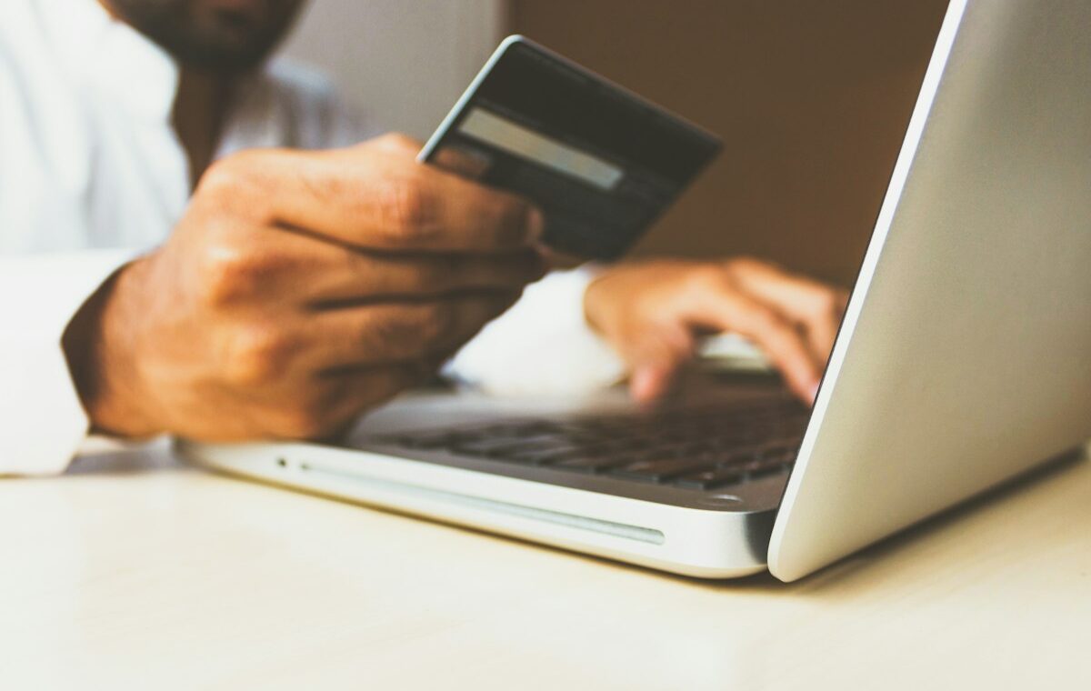 Person holding a credit card beside a laptop for an online purchase