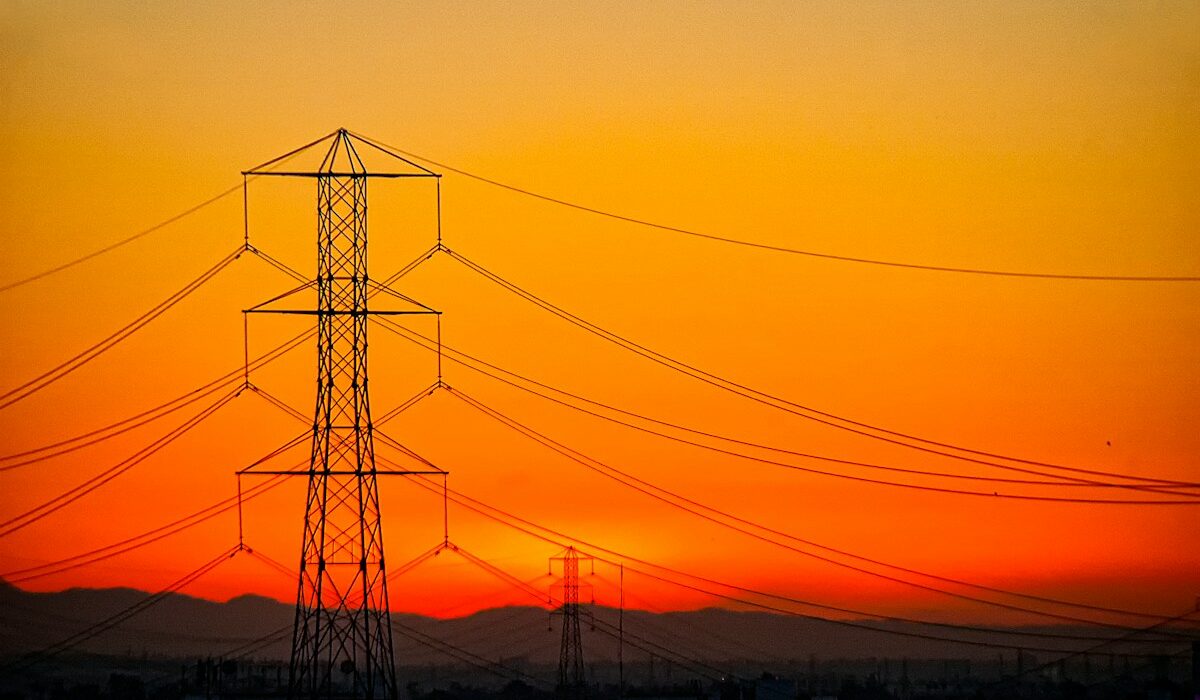 Electric transmission lines silhouetted against an orange sunset