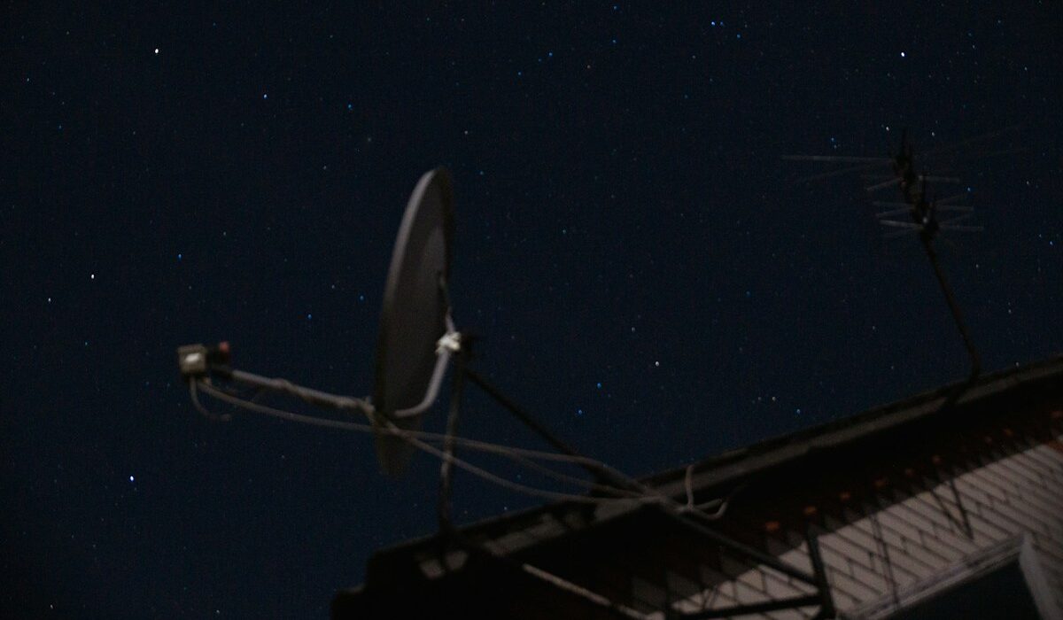 Starlink Mobile spectrum expansion represented by a rooftop satellite dish beneath a clear night sky.